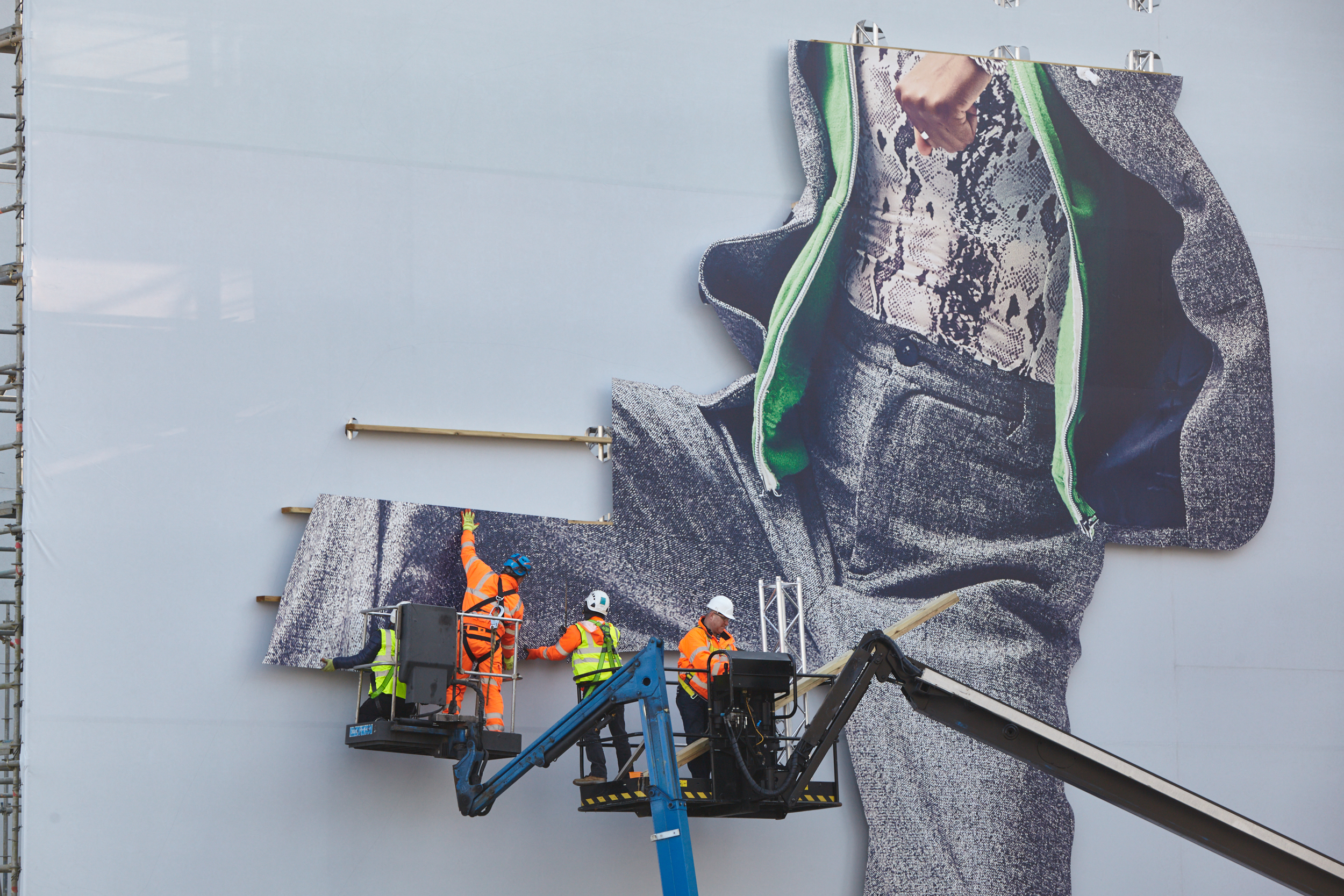 Apple Airpods Pro OOH installation being built by a team of builders on a large cherry picker truck in the process of building the massive motif of a man kicking his leg out of the build.