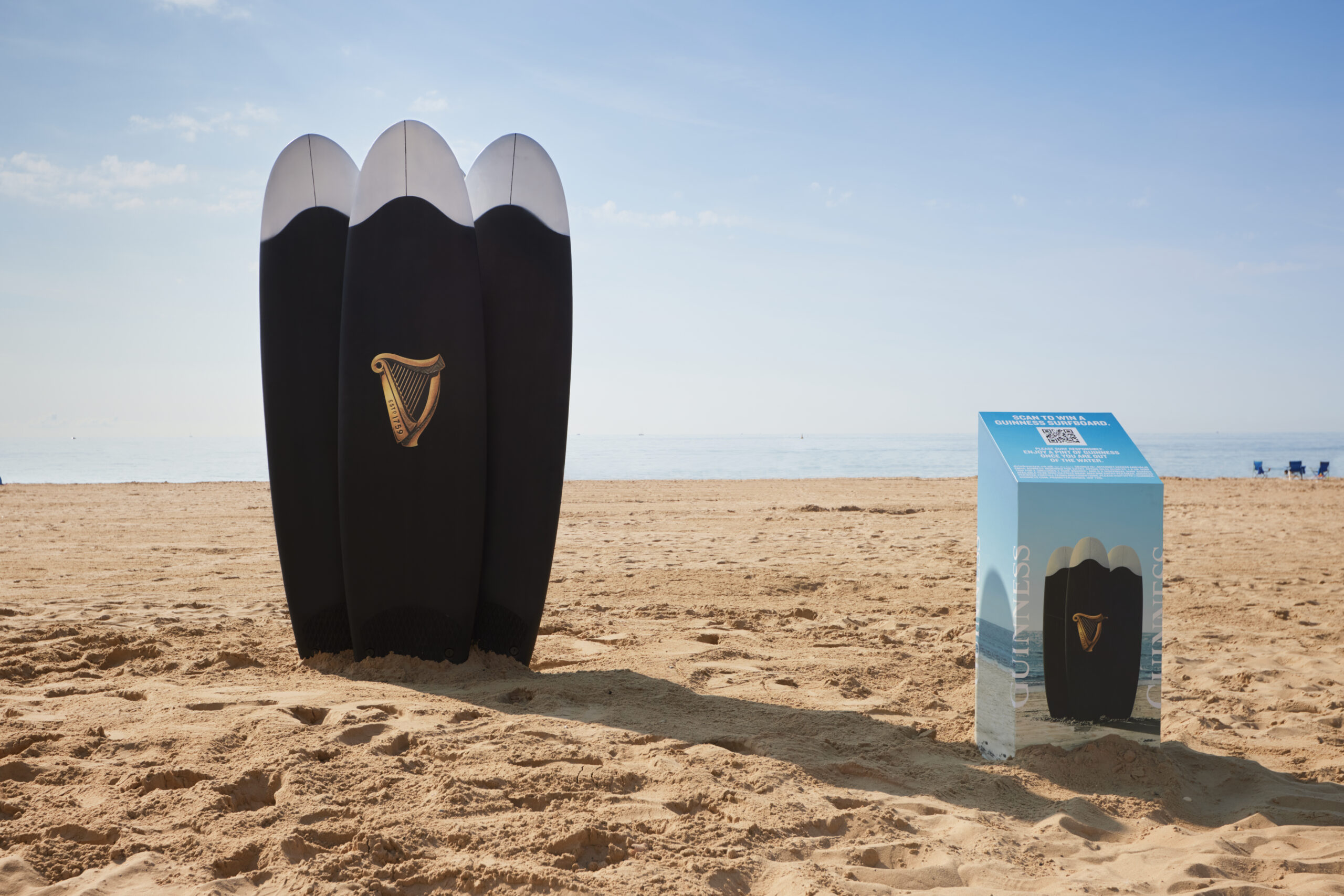 Three black surfboards with the Guinness logo stand on Bournemouth Beach.